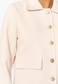 Gaiši rozā teksturēta jaka ar apkakli, priekšējo kabatu un zeltainiem pogu akcentiem. Piemīt pieguļošs siluets un gludas līnijas.