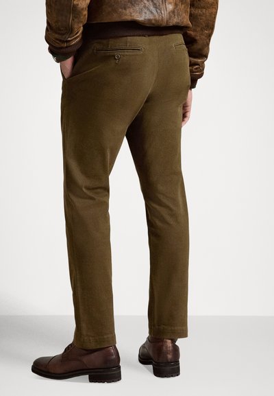 Παντελόνια ελιάς με στενή γραμμή, κατασκευασμένα από λείο ύφασμα. Διαθέτουν δύο πίσω τσέπες, η μία με κουμπί κλεισίματος, και στενή γραμμή στο πόδι.