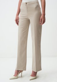 Pantaloni beige a gamba dritta realizzati in misto cotone, con una texture liscia e chiusura frontale con bottone, abbinati a tacchi a punta bianchi.
