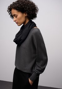 Ciemnoszary, dziergany sweter o luźnym kroju i długich rękawach, zestawiony z czarnym, marszczonym szalikiem, na neutralnym tle.