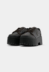 Masywne czarne skórzane sneakersy z grubymi podeszwami o wyraźnym bieżniku i sznurowanym przodem na białym tle.