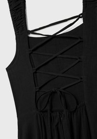 Robe noire avec un corsage ajusté et de fines bretelles. Elle présente un dos à lacets croisés et des détails froncés à la taille pour la texture.