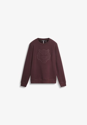 Bordo dukserica s podignutim grafičkim prikazom tigrove glave na sredini. Izrađena od mekog materijala, s dugim rukavima i rebrastim manžetama.