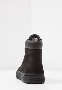 Černá kožená kotníková bota s polstrovaným límcem, texturovaným povrchem a gumovou podrážkou. Logo Timberland je na boku vyraženo.
