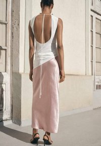 White sleeveless top with an open back and a tie detail, paired with a flowing pink satin skirt. Black heeled sandals complete the look.