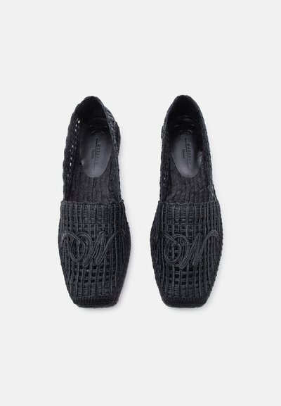 Chaussures à enfiler tissées noires avec semelles plates et un motif décoratif cousu à l'avant, vues de dessus sur un fond blanc.