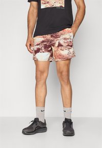 Nike-Shorts mit einem mehrfarbigen abstrakten Muster in Braun-, Creme- und Orangetönen, kombiniert mit grauen Nike-Socken und schwarzen Schuhen.