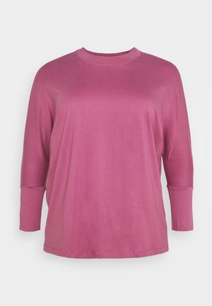 Camiseta de manga larga, de corte holgado y cuello redondo en color rosa polvo sólido, mostrada sobre un fondo blanco liso.