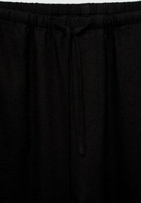 Pantalons noirs à taille élastique avec cordon de serrage. Fabriqués en tissu texturé, présentant une coupe ample et un design simple et minimal.