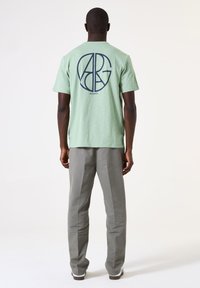 Groen katoenen T-shirt met een marineblauw logo ontwerp op de achterkant, gecombineerd met lichtgrijze broeken. Eenvoudig en recht gesneden ontwerp.
