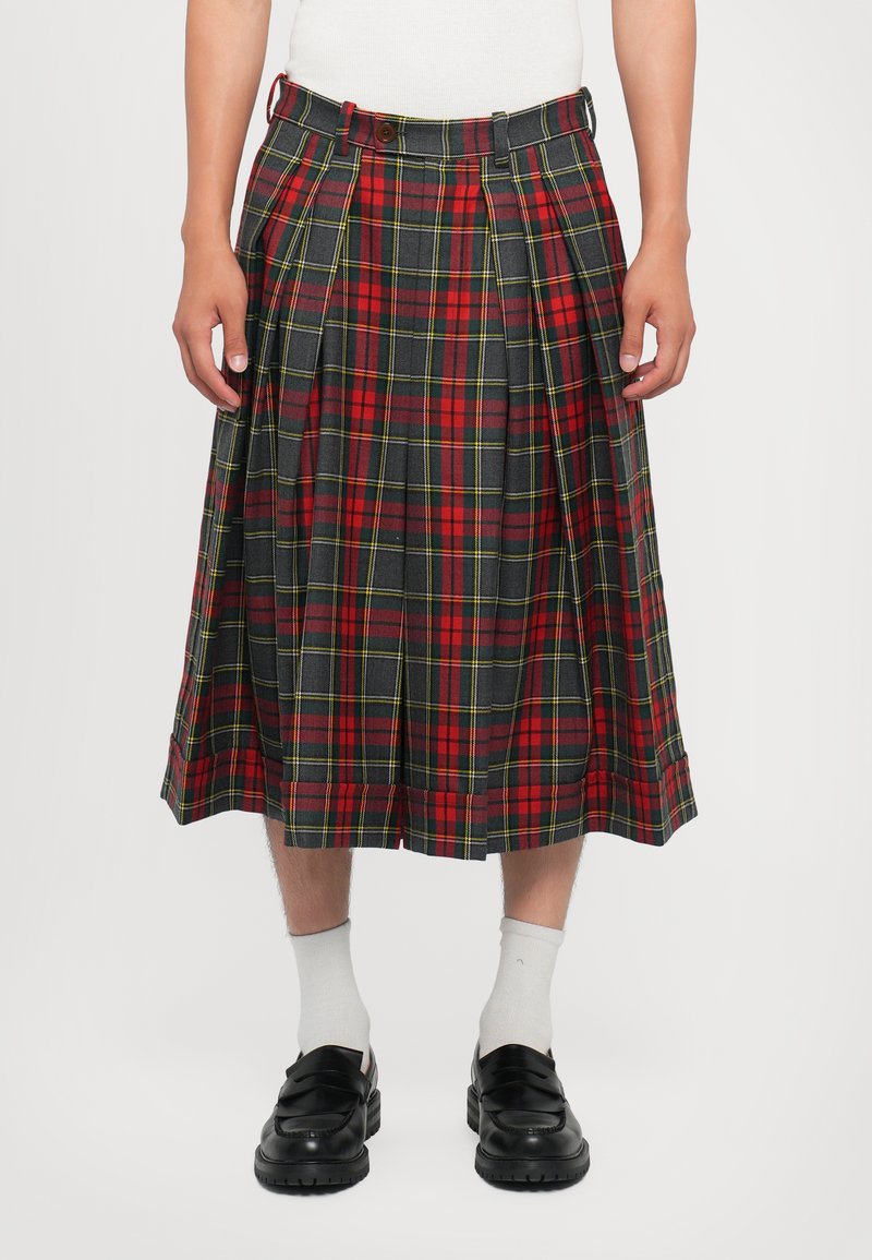Karierter Tartan-Kilt mit rotem, grünem und gelbem Muster, Falten, einem knopfverzierten Bund und knielangem Design. Getragen mit schwarzen Schuhen und weißen Socken.
