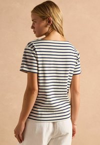 Kreemivärvi triibuline lühikeste varrukatega topp, millel on tumehalli sinised triibud. Omab avarat kaelust ja keha lähedast lõiget. Materjal näib olevat pehme ja kerge.