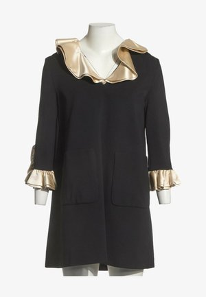Robe noire à manches longues avec col et poignets volantés en satin beige, avec deux poches plaquées devant sur un mannequin blanc.