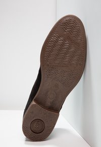 Baskets noires avec une semelle texturée, dotées d'une semelle extérieure en caoutchouc marron et d'un marquage discret. Matière lisse et durable avec un design minimaliste.