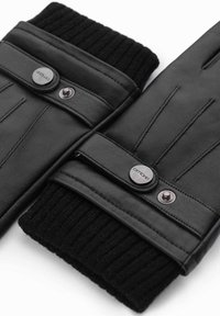 Une paire de gants en cuir noir avec des poignets en tricot côtelé et des sangles à bouton-pression sur un fond blanc.