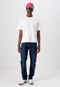 White cotton t-shirt, dark blue denim jeans, red cap, and gray sneakers with black and white accents. Simple design, casual fit.