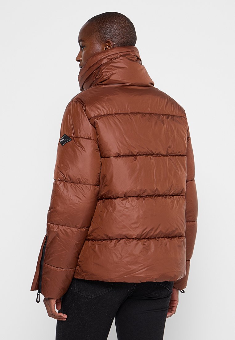 Giacca a vento marrone con colletto alto, texture trapuntata, zip laterali e patch con logo sulla spalla sinistra.