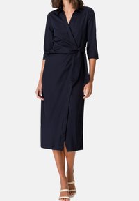 Vestido envolvente azul marino con cuello, mangas tres cuartos y cintura atada. Tejido suave con una abertura hasta la rodilla en la parte delantera.