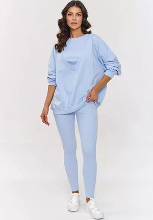 Jasnoniebieski, oversize sweatshirt z okrągłym dekoltem, zestawiony z jasnoniebieskimi, prążkowanymi legginsami. W komplecie białe trampki dla casualowego wyglądu.