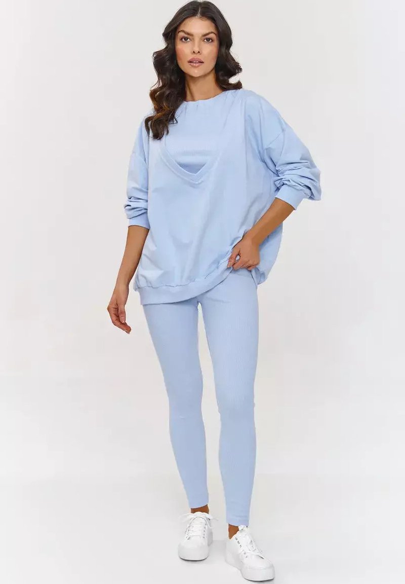 Jasnoniebieski, oversize sweatshirt z okrągłym dekoltem, zestawiony z jasnoniebieskimi, prążkowanymi legginsami. W komplecie białe trampki dla casualowego wyglądu.