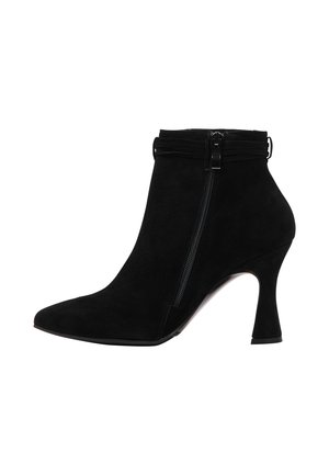 Stivale alla caviglia in suede nero con punta affusolata, chiusura con zip e tacco a campana. Presenta una superficie testurizzata e accenture di design minimaliste.