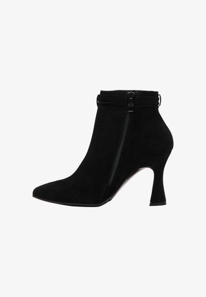 Stivale alla caviglia in suede nero con punta affusolata, chiusura con zip e tacco a campana. Presenta una superficie testurizzata e accenture di design minimaliste.