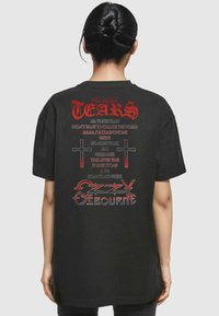 Schwarz T-Shirt aus Baumwolle mit roter und weißer Schrift auf der Rückseite, einschließlich der Phrase "KEINE TRÄNEN MEHR" und einer Grafik von zwei Kreuzen.