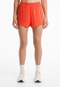 Shorts de sport rouges avec une taille élastique, en tissu léger et lisse, avec une coupe ample et des ourlets arrondis. Assortis à des baskets légères et des chaussettes.