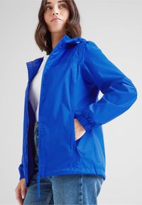 Blue lightweight jacket with a hood, elastic cuffs, and side pockets. Smooth material with a slightly shiny finish, featuring a front zipper.