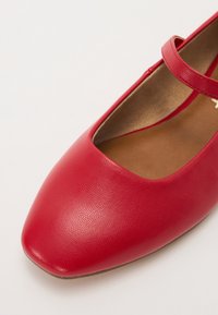 Zapato plano de cuero rojo con punta cuadrada y correa en el tobillo, con una textura suave y una plantilla acolchada para mayor comodidad.