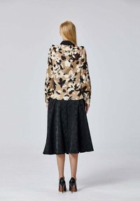Blouse florale beige avec des accents noirs et blancs, associée à une jupe noire à mi-longueur avec un motif texturé ; chaussures à talons noirs.