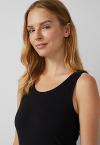 Débardeur noir avec un décolleté en scoop, fabriqué en tissu lisse. Dispose de fins bretelles et d'une coupe ajustée, mettant en valeur les épaules.