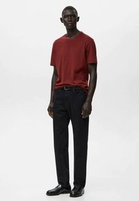 Czerwona koszulka z okrągłym dekoltem zestawiona z czarnymi spodniami. Strój cechuje się prostym wzorem, gładką fakturą i schludnym krojem. Całość dopełniają czarne buty.