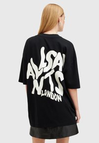 Černé oversize tričko s výraznou bílou typografií "ALLSAINTS LONDON" v rozteklém stylu na zadní straně. Měkká tkanina s krátkým rukávem.