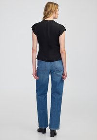 Top nero a maniche corte con scollatura aderente e dettaglio della zip sul retro, abbinato a jeans blu a gamba dritta e stivali neri con tacco.