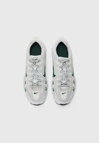 Sneakers bianchi con accenti verdi, tomaia in rete e sintetico, design con lacci, colletto imbottito, con un logo di marca prominente sul lato.