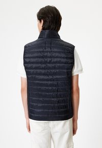 Navy blue quilted vest with a high collar, featuring horizontal stitching patterns and a smooth texture. Back view shows armholes and tailoring.