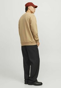 Beige sweatshirt with ribbed cuffs, paired with loose black trousers and black shoes. The person is wearing a red cap.