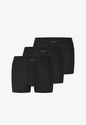 Tre sorte boksershorts til mænd stablet, med elastiske taljebånd og synlige forreste syninger.