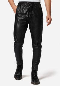 Zwarte leren joggerbroeken met een trekkoord in de taille, slim fit, met ritsen bij de enkels en zijzakken, gecombineerd met zwarte laarzen.