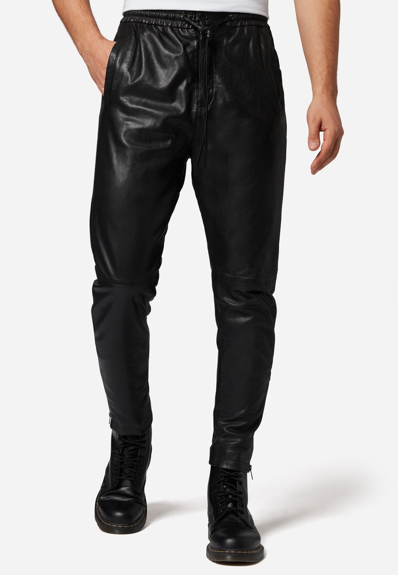 Zwarte leren joggerbroeken met een trekkoord in de taille, slim fit, met ritsen bij de enkels en zijzakken, gecombineerd met zwarte laarzen.