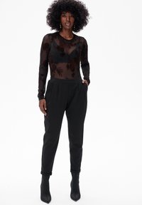 Zwarte doorschijnende longsleeve bodysuit met bloemenborduurwerk, gecombineerd met zwarte high-waisted tapered broeken en zwarte puntige enkellaarsjes.