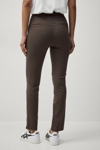 Pantalons moulants bruns avec une taille élastique ; comportent deux poches arrière ; portés avec des baskets blanches avec des accents noirs.