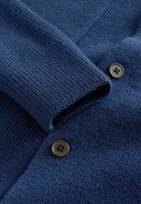 Ciemnoniebieski sweter z dzianiny o prążkowanej fakturze, z brązowymi guzikami. Zbliżenie pokazuje miękką tkaninę i detale guzika.