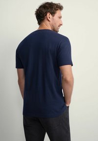 Granatowa koszulka z krótkim rękawem, wykonana z miękkiej bawełny, z okrągłym dekoltem i subtelną teksturą. Widok z tyłu, noszona z ciemnymi dżinsami.