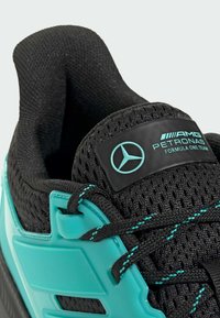 Chaussure de sport noire avec une tige en mesh, des accents turquoise et une étiquette brillante noire de marque avec un logo. Design à lacets avec des détails texturés.