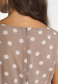 Braunes Polka-Dot-Kleid mit quadratischem Ausschnitt, ausgestattet mit einem versteckten Reißverschluss auf der Rückseite und aus leichtem Stoff.
