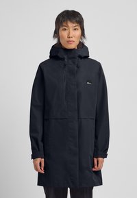 Dunkelblauer wasserdichter Parka mit verstellbarer Kapuze, Fronttaschen und einem Logo-Patch auf der linken Brust. Glattes, langlebiges Material.