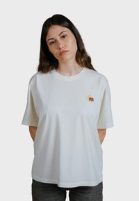 Bílý bavlněný tričko s kulatým výstřihem. Obsahuje vyšívaný design v oranžové a žluté barvě na levé hrudi. Pohodlný střih, krátké rukávy.