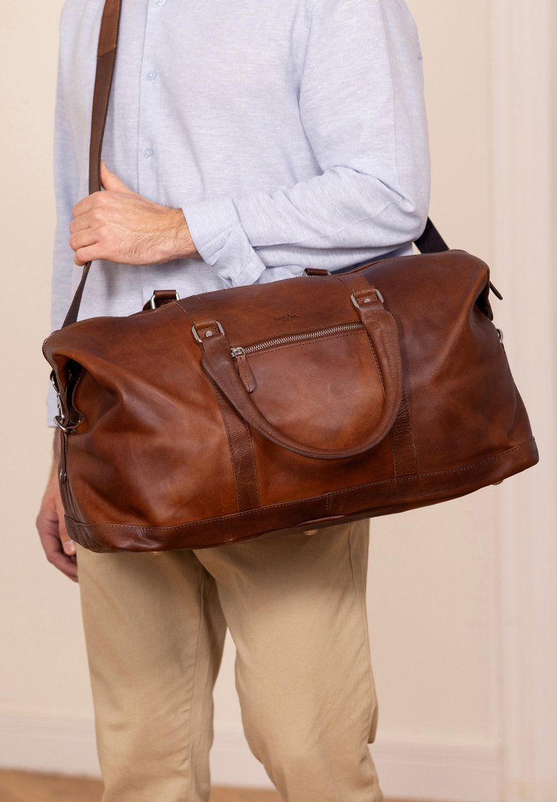 Rjava usnjena torba za potovanje z gladko teksturo, dvojni ročaji, nastavljiv trak za ramo in sprednji žep z zadrgo.